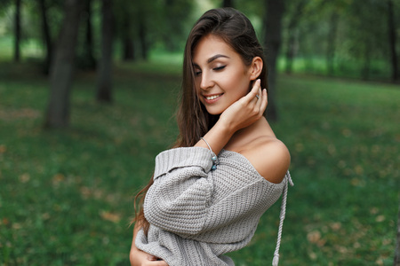 Beautiful happy young woman smiling in a gray sweater in a green park.の写真素材