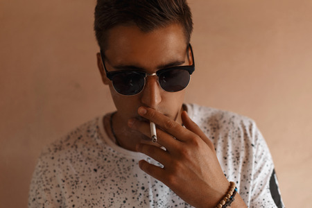 Young hipster man with sunglasses and hairstyle smoking a cigarette.の写真素材