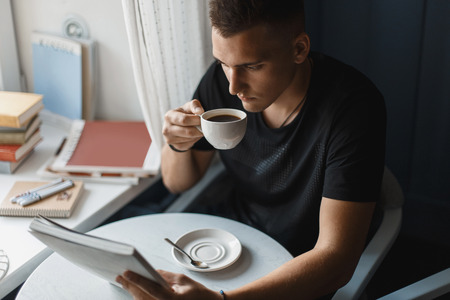 Young man reading a book and drinking coffee in a restaurant