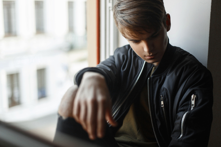 Handsome young man model sits on the windowの写真素材