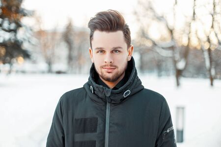 Handsome man with a beard and hairstyle in winter jacket in the park