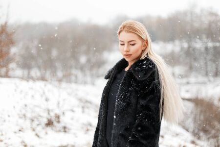 Beautiful young blonde girl in fur coat posing in winter parkの写真素材