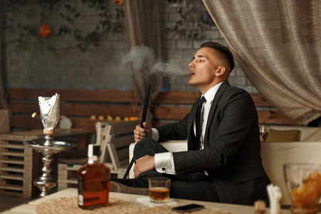 Handsome young man in an expensive dress smokes a hookahの写真素材