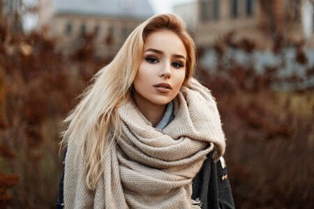 Beautiful young woman in a warm scarf standing in autumn park.