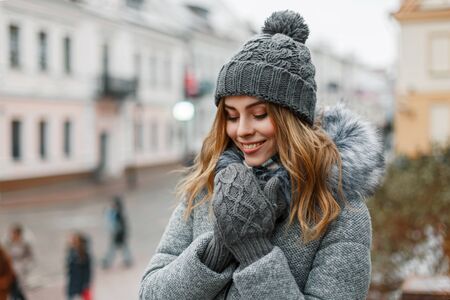 Pretty woman smiling in a knitted hat and a mittens on a background of the city.の写真素材