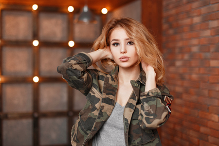 Stylish beautiful young woman in a fashionable jacket near wall with lightsの写真素材