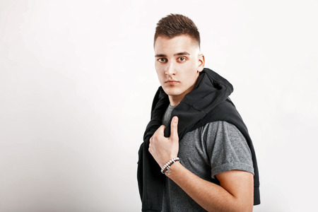 Fashionable young man with hairstyle in a gray shirt and a black cardigan on a white background