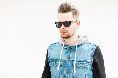 Portrait of a young guy with sunglasses and a denim vest near the wallの写真素材