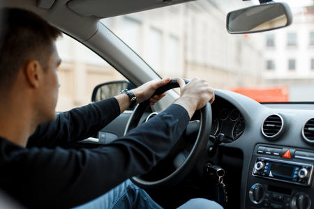 Young male driver sitting in the car and holding the wheelの写真素材