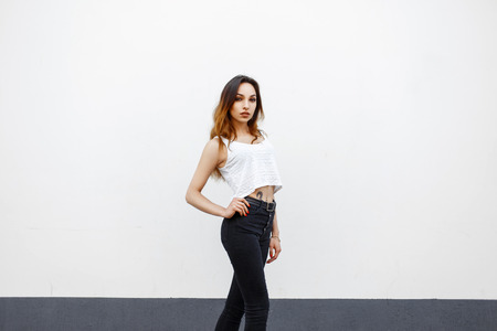 Beautiful young woman with a slender body with black high jeans and a white tank top near the wallの写真素材
