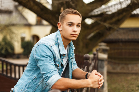 Handsome stylish man in jeans clothes and a white T-shirt near a house in the gardenの写真素材
