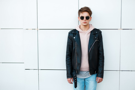 young man in a black leather jacket and a pink sweatshirt near a white wall. Vintage sunglasses aviatorの写真素材