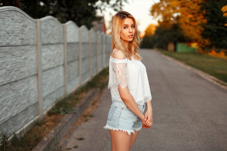 Beautiful sexy model blonde woman in a white lace T-shirt with jeans shorts on a summer day in the parkの写真素材