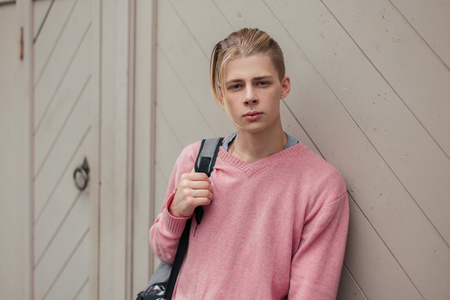 Handsome stylish young guy with a backpack near the wallの写真素材
