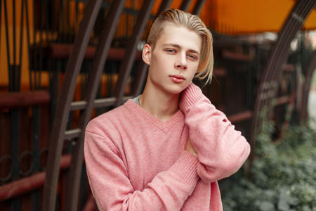 Handsome young model man with a blond hairstyle in a pink sweater on the streetの写真素材