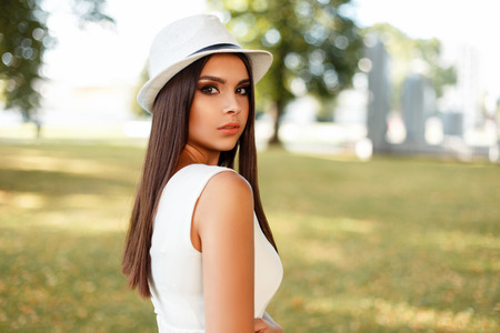 Fashionable beautiful young woman in a white dress with a hat outdoors in the parkの写真素材