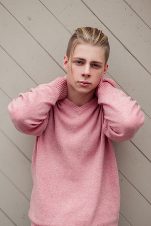 handsome young man with blond hair in a fashion pink sweater near a wooden wallの写真素材