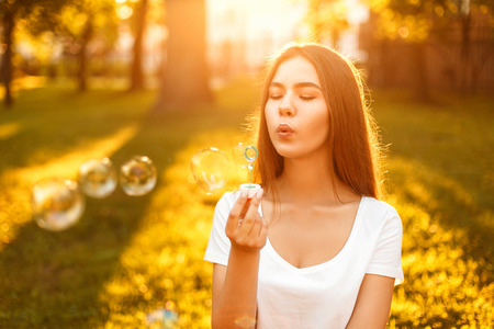 Happy young beautiful woman with soap bubbles resting in the park at sunsetの写真素材