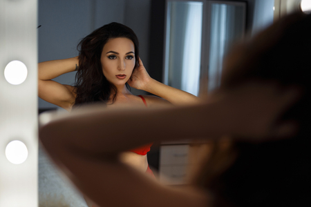 Fashionable beautiful sexy woman with a hairstyle in underwear looks in the mirrorの写真素材