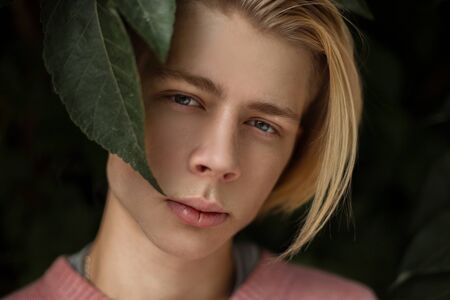 Natural portrait of a handsome young man with a blonde hairstyle in the foliageの写真素材