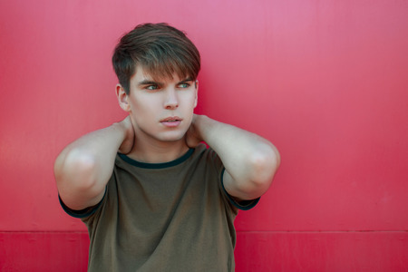 Handsome young man in a classic T-shirt posing near a pink wallの写真素材