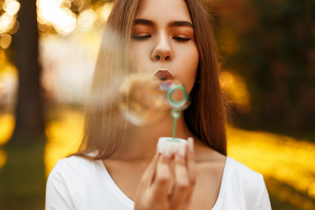 Beautiful young happy girl with soap bubbles in the park at sunsetの写真素材