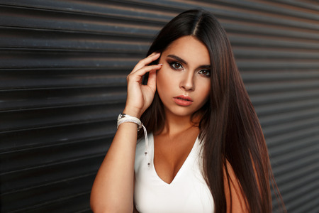 Beautiful fashionable young woman with make-up in a white dress near the metallic roller blindsの写真素材
