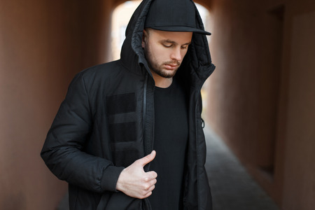 Fashionable handsome young man with a black baseball cap in a hood with a winter jacket on the...