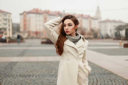 Fashionable beautiful young woman in trendy coat posing in the city on a fall dayの写真素材