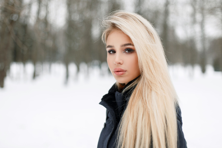 Fashionable beautiful young woman in a trendy elegant coat in the park on a winter snowy dayの写真素材