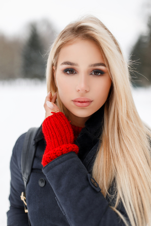Beautiful young stylish girl model in a stylish elegant coat with a bag on a winter snowy day in the parkの写真素材
