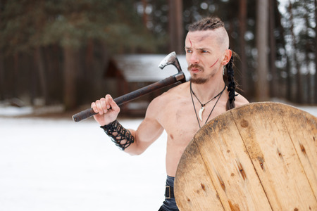 Viking man with a scar with an ax and a shield in the woods on a winter dayの写真素材
