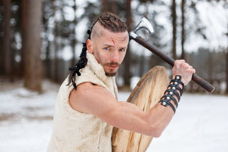 Viking warrior with an ax and a wooden shield in the forest on a winter dayの写真素材