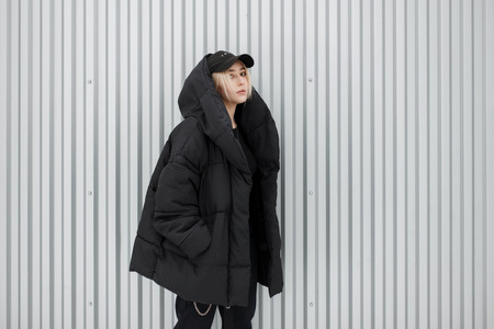 Stylish beautiful fashionable young model girl in a black winter jacket with a fashion black cap...