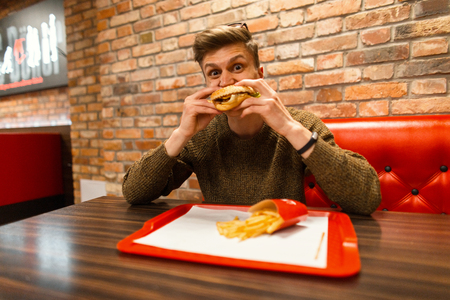 Handsome young man eats fast food. Hamburger and French friesの写真素材