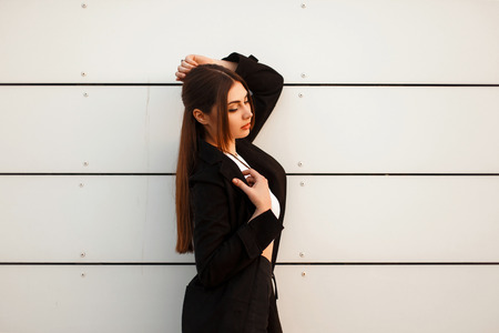 Fashion model in black coat posing near white wallの写真素材