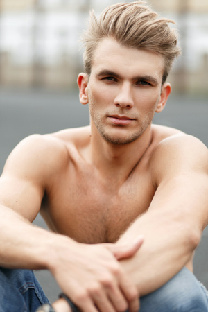 Fresh portrait of a handsome fit young man with a hairstyle with a naked healthy body sits on the streetの写真素材
