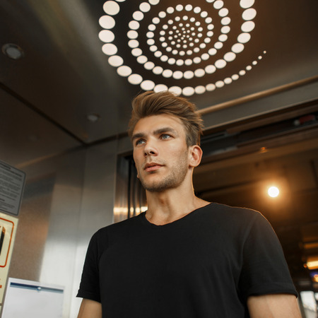 Fashionable portrait of a handsome young man with a haircut in a black T-shirt in an elevator