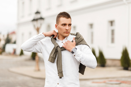 Handsome young successful man in a white shirt with a sweater posing in the city
