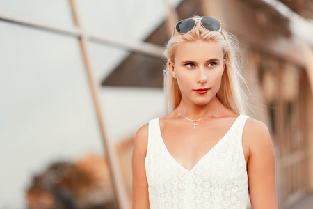 Young beautiful blonde girl with sunglasses in a fashion white summer dress on the streetの写真素材