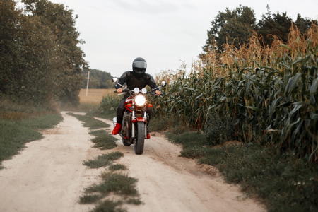 man with a helmet and black outfit travels by motorcycle on a country road in a cornfieldの写真素材