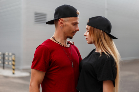 Beautiful young stylish hipster couple with baseball caps in fashionable clothes stands on the streetの写真素材