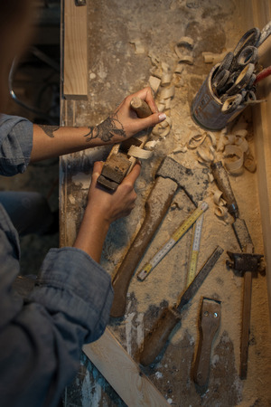 Female hands with tattoos make a wooden product in the workshop. View from aboveの写真素材