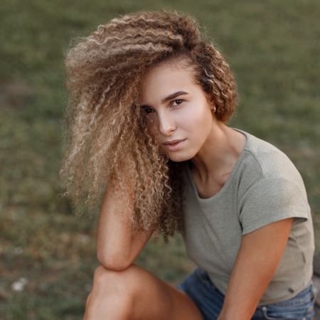 Outdoor portrait of a beautiful young stylish woman with curly hairstyle in a fashion t-shirt