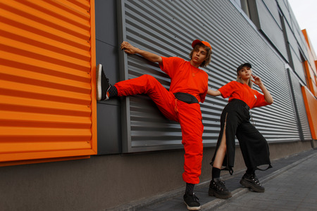 Funny beautiful fashionable young couple in stylish bright orange clothes with fashion cap posing near the metallic gray-yellow wallの写真素材