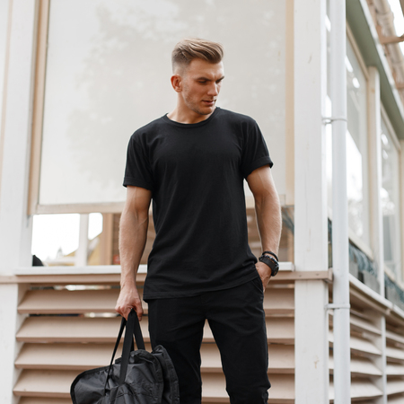 Stylish handsome young american hipster model man with hairstyle in black t-shirt with fashion bag...