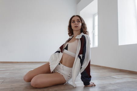 Stylish beautiful young girl in fashionable sportswear with shorts sits on the floor in the roomの写真素材