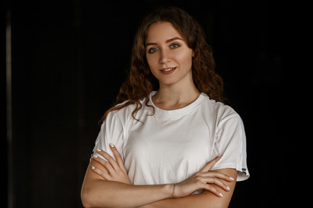 Beautiful young happy girl with a natural make-up with a smile in a white T-shirt on a dark backgroundの写真素材