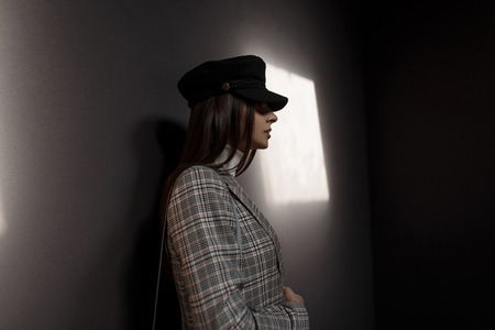 Profile of beautiful young woman in vintage fashion checkered suit and stylish hat on dark background with lightの写真素材