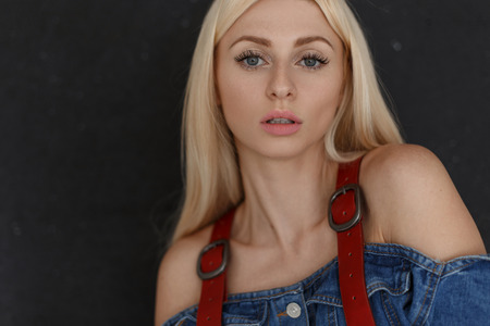 Fashionable portrait of a beautiful young attractive woman with freckles and natural make-up in stylish vintage denim clothes on a black background.の写真素材